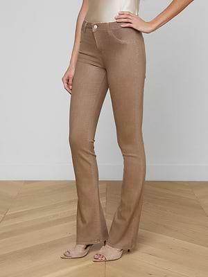 Wearing the Selma Coated Bootcut Jean in light brown and open-toe nude heels, a person stands on a wooden floor against a white wall, torso partially visible with one hand on their hip.