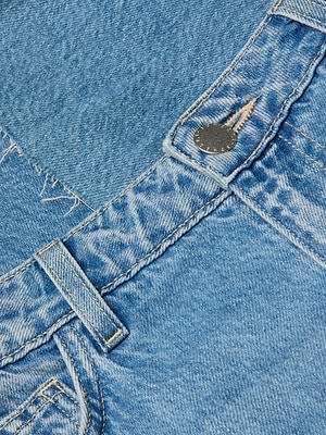Close-up of the Wanda Cropped Wide-Leg Jean in blue denim, highlighting the waistband, belt loop, metal button, and faded stitching. The worn texture and relaxed silhouette bring effortless Parisian style to this wide-leg jean.