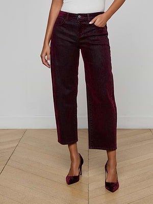 A person wears L'AGENCE Dolores Flocked Bow-Leg Jeans in dark bordeaux with a white top and matching pointed-toe heels, standing on a light wooden floor against a plain white wall.