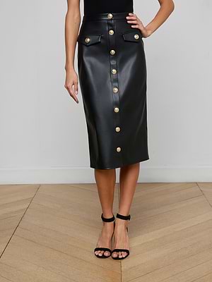 A woman styles the L'AGENCE Milann Vegan Leather Skirt, featuring gold accent buttons and flap pockets, with a black sleeveless top and high-heeled sandals for a chic, modern look.