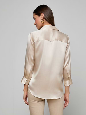 A woman with straight brown hair wears the Dani Silk Blouse—a champagne silk charmeuse, long-sleeve button-down—paired with gold hoop earrings, shown from the back against a plain light gray background.