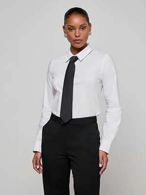 A woman wears the Blake Bodysuit, featuring a removable tie, with black pants. She stands confidently against a plain light gray background, looking at the camera with her hands by her sides.