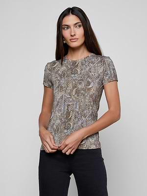 Woman with long brown hair wears the bestselling Ressi Fitted Tee, featuring a neutral paisley print, paired with black pants. She stands against a light gray background, looking to the side with her hands clasped in front.