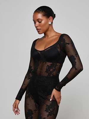 A woman poses against a plain background wearing the Gwendolyn Mesh Knit Bodysuit by L'AGENCE, featuring sheer black mesh with floral patterns. Her hair is pulled back, she looks down, and wears stud earrings.
