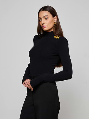 A woman with long brown hair wears the L’AGENCE Jennis Mock-Neck Bodysuit with gold shoulder buttons and black pants, posing against a plain light gray background.