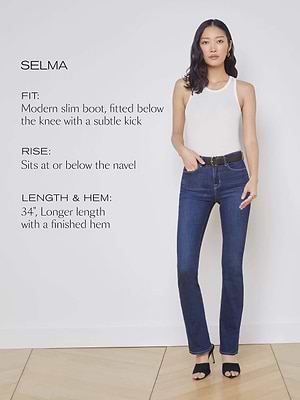 A woman in a white sleeveless top and dark blue Selma Bootcut Jean by L'AGENCE stands against a white wall. Text beside her highlights the high-rise fit, rise, length, and hem details of the jean.
