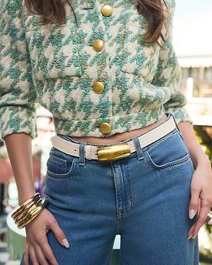 Person wearing a green patterned jacket with gold buttons and blue jeans.