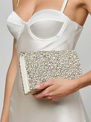 A woman in a white satin dress holds the Verve Crystal Clutch, adorned with handcrafted crystals, making it the perfect statement accessory at her side.