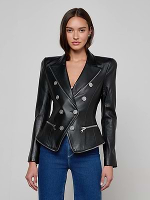A woman with straight brown hair and a neutral expression models the L'AGENCE Ottilie Leather Blazer—an Italian lambskin piece with silver buttons and front zippers—paired with blue jeans against a plain background, expressing effortless power dressing.