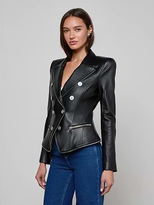 A person stands against a plain background wearing the Ottilie Leather Blazer by L'AGENCE, featuring Italian lambskin, silver buttons, and zipper details, paired with blue jeans for a modern power dressing look.